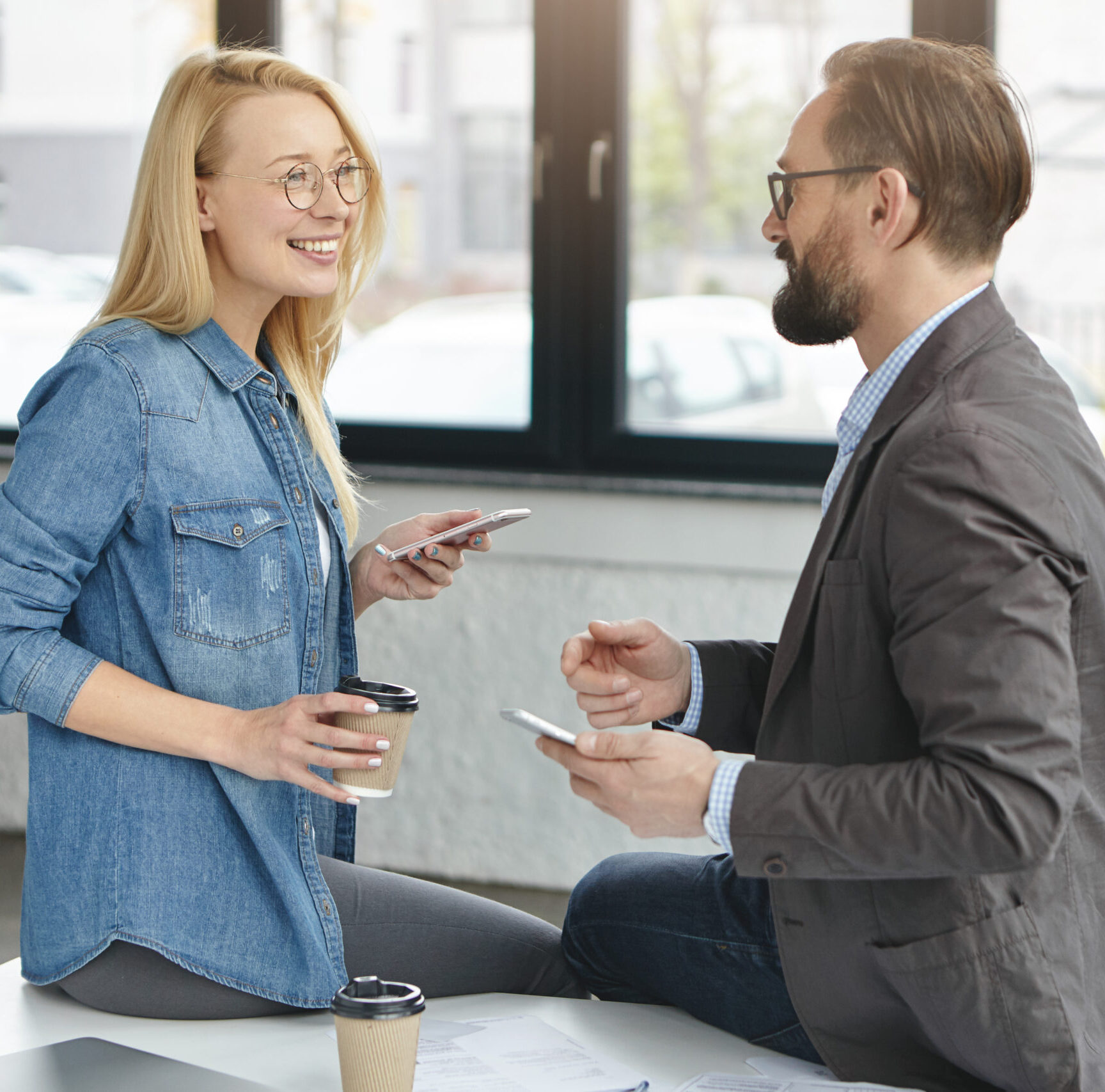 friendly business partners have informal meeting, chat during coffee break, use modern mobile phones for keeping in touch, connected to wireless internet, sit at working table. career concept